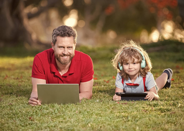 dad and son use laptop for video call or lesson listen music in headphones in park, family. - Zdjęcie, obraz