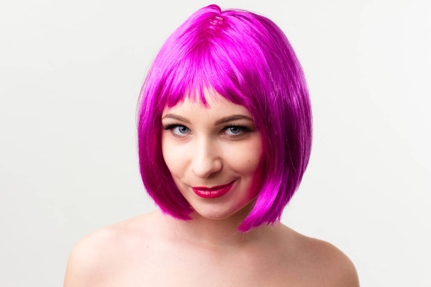Rosto de uma jovem mulher com maquiagem brilhante em um fundo rosa com cabelo reunido em um rabo de cavalo liso. - Foto, Imagem