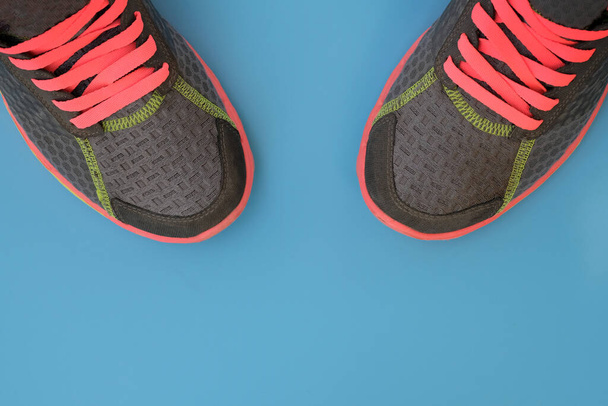 Серые кроссовки с розовыми шнурками вид сверху. Спортивная обувь с яркими шнурками на синем фоне. Кроссовки за побег. Концепция активного образа жизни, утренние пробежки, спорт. - Фото, изображение