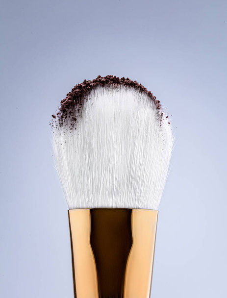 Brush tip with white bristles and brown product sprinkled on top. Macro photo on a light background - Фото, зображення