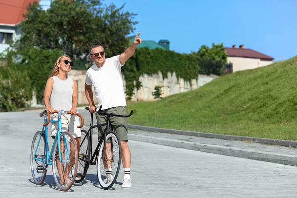 Pareja adulta con bicicletas caminando en el parque de la ciudad en el día de verano - Foto, Imagen