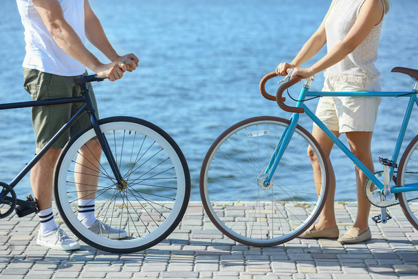 Зрелая пара с велосипедами прогуливается вдоль берега реки в летний день - Фото, изображение