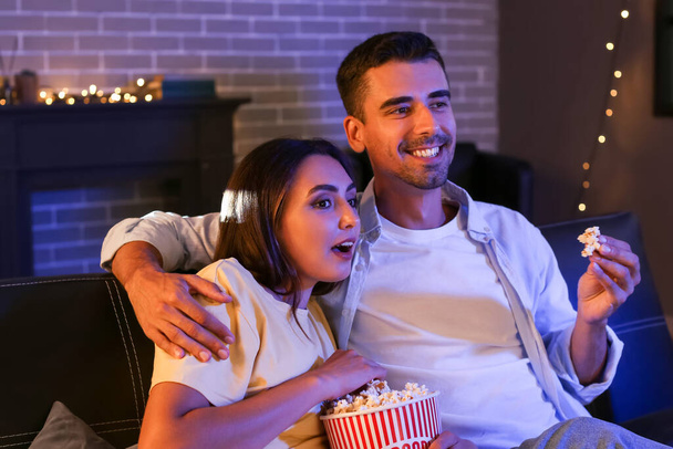 Happy young couple with popcorn watching movie at home in evening - Foto, immagini