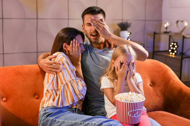 Scared family with popcorn watching movie at home in evening - Fotoğraf, Görsel