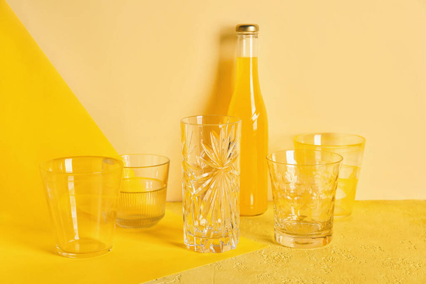 Stijlvolle lege glazen en flesje sap op oranje achtergrond - Foto, afbeelding