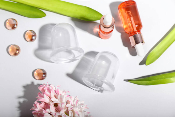 Вакуумні банки для антицелюлітного масажу, пляшки ефірної олії та квітка гіацинта на білому тлі
 - Фото, зображення