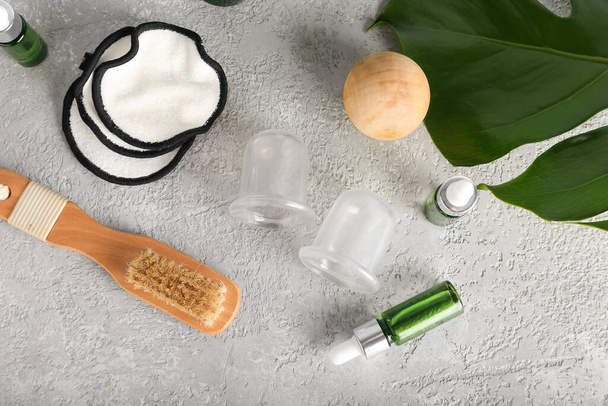 Composition with vacuum jars for anti-cellulite massage, bottles of essential oil, brush and cotton pads on grunge background - Photo, image