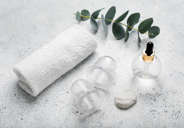 Composition with bottle of essential oil, clean towel and vacuum jars for anti-cellulite massage on light background - Photo, Image
