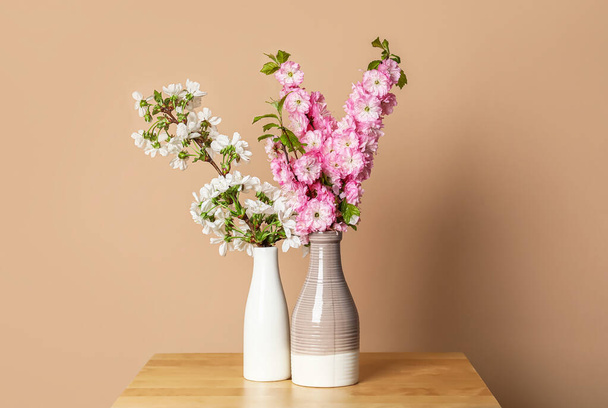 Ceramic vases with beautiful blooming branches on table near beige wall - Photo, image