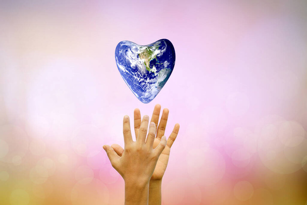 Earth conservation concept. The world of hearts floats above human hands. nature blur background - Foto, Imagen