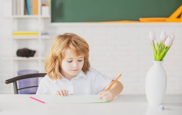 Pupil doing lessons at home. School kid writing something in copybook and sitting at table in classroom. First grader. - Фото, изображение