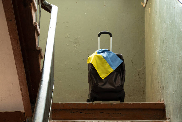 Ein Koffer mit der Flagge der Ukraine steht im Eingang des Hauses, Menschen verlassen ihre Heimat wegen des Krieges, ukrainischer Flüchtlinge, des Krieges in der Ukraine, eines Koffers und der Reise - Foto, Bild