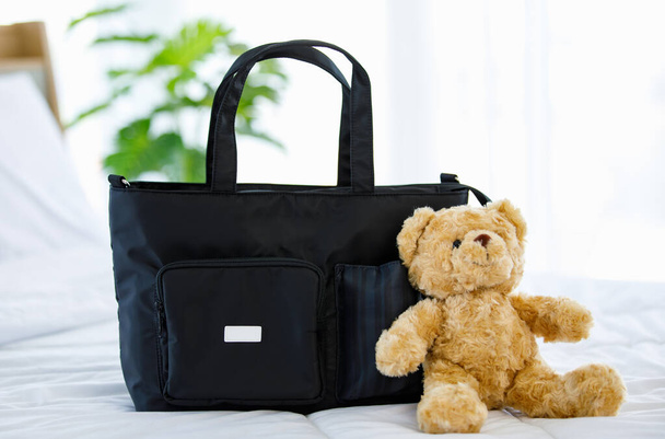 Primer plano de estudio de color negro multifunción utilidad multiusos recién nacido accesorios para niños bolso de mano en la cama con muñeca de oso de peluche - Foto, Imagen