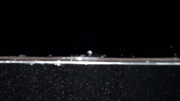 Pequeñas burbujas de aire de cámara lenta en el agua que sube a la superficie sobre fondo negro - Metraje, vídeo