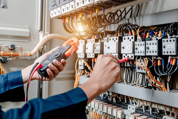 Ingeniero electricista utiliza un multímetro para probar la instalación eléctrica y la corriente de la línea de alimentación en un gabinete de control del sistema eléctrico. - Foto, imagen