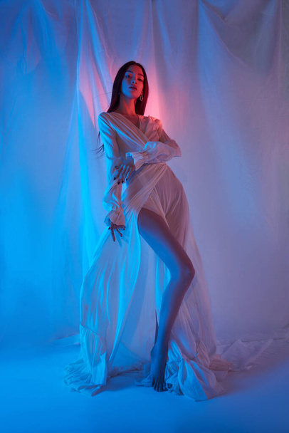 Beauty fashion woman in light white dress in studio. Freedom concert in neon color light. Fashion style light dress on body woman, long legs - Photo, image