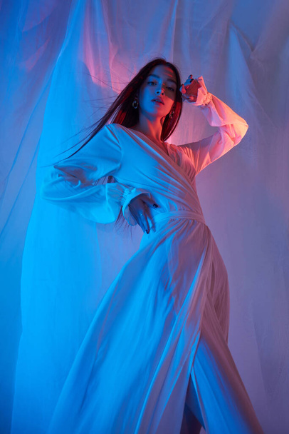 Beauty fashion woman in light white dress in studio. Freedom concert in neon color light. Fashion style light dress on body woman, long legs - Valokuva, kuva
