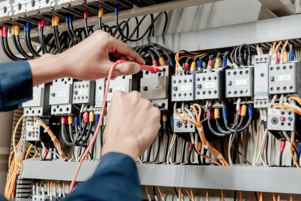 Electrician engineer uses a multimeter to test the electrical installation and power line current in an electrical system control cabinet. - Фото, изображение