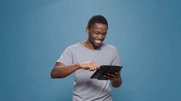 Νεαρός ενήλικας γελάει με την εφαρμογή social media στην ψηφιακή ταμπλέτα - Φωτογραφία, εικόνα