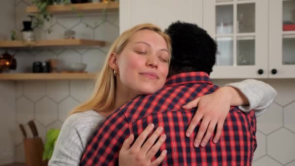 Smiling caucasian woman girlfriend hugs African American man boyfriend at home - Filmati, video