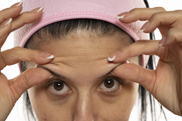 μεσήλικη γυναίκα που δείχνει τις ρυτίδες του μετώπου της με τα δάχτυλά της σε λευκό φόντο - Φωτογραφία, εικόνα