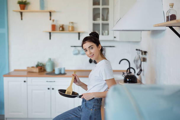 Szczęśliwy atrakcyjny młody gotowanie kobieta gospodyni przygotowuje jedzenie w patelni na pyszny obiad w nowoczesnym stylu loft kuchnia - Zdjęcie, obraz