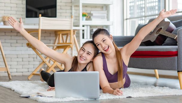 Two millennial Asian young healthy slim strong sexy female sporty models in casual crop top sportswear laying down on carpet floor learning yoga pilates lesson from laptop notebook computer together. - Fotografie, Obrázek