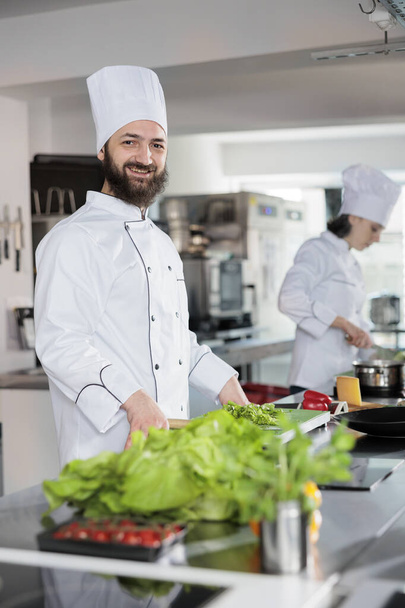 Portrait of happy head chef wearing cooking uniform, standing in restaurant professional kitchen - Fotografie, Obrázek