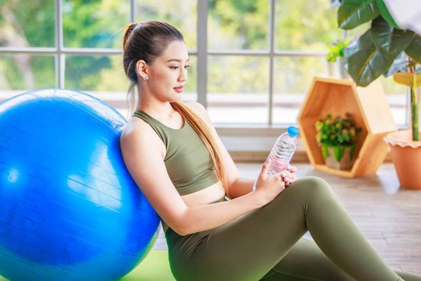 Closeup shot of Millennial Asian young healthy slim strong sexy female sporty model in casual crop top sportswear sitting on exercise ball smiling posing holding hand at chin in classroom gym studio. - Foto, imagen