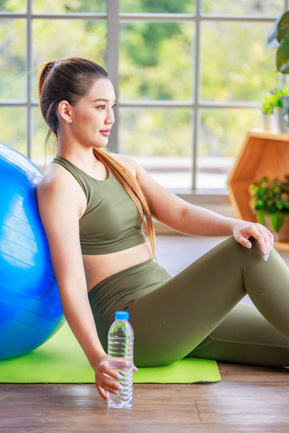 Closeup shot of Millennial Asian young healthy slim strong sexy female sporty model in casual crop top sportswear sitting on exercise ball smiling posing holding hand at chin in classroom gym studio. - Photo, image