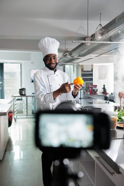 Travailleur de l'industrie alimentaire avec poivron jaune enregistrement cours culinaire dans la cuisine professionnelle restaurant. - Photo, image