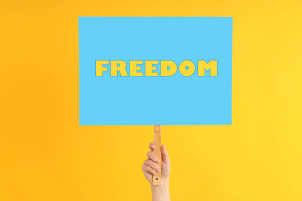 Female hand holds protest sign with text Freedom on yellow background - Foto, imagen