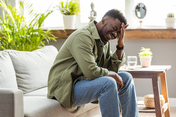 Closeup of young african american man suffering from headache at home, touching his temples, copy space, blurred background. Migraine, headache, stress, tension problem, hangover concept - Foto, imagen