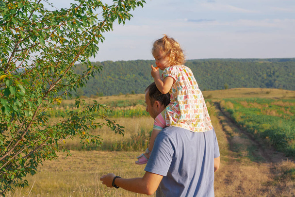 Otec s dítětem na ramenou v zahradě. Rodina v přírodě v obci koncept. - Fotografie, Obrázek