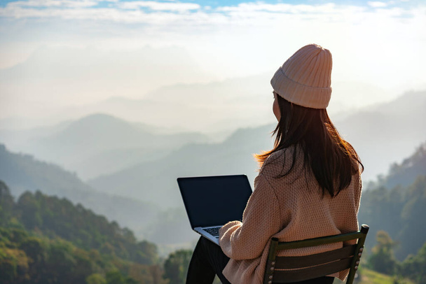 Young woman freelancer traveler working online using laptop and enjoying the beautiful nature landscape with mountain view at sunrise - Foto, Imagem