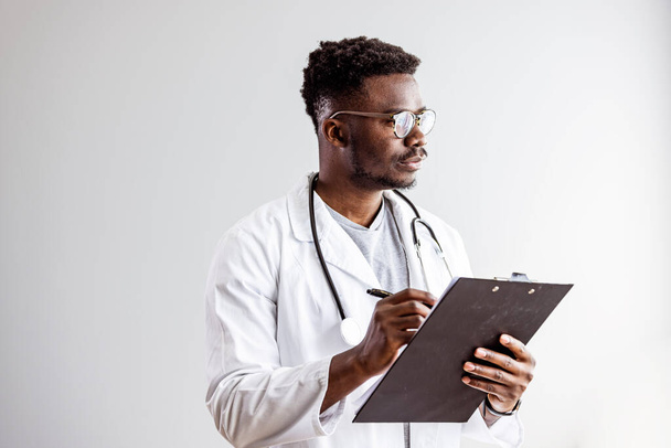 Portrait of smiling black male doctor with stethoscope on white background. Young happy black medical doctor holding medical chart over white studio background, copy spac - Zdjęcie, obraz