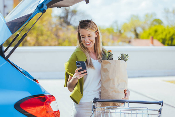 young woman with shopping bag using smartphone near car - Foto, Bild