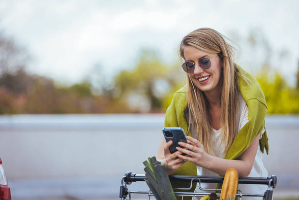 young woman with shopping cart and smartphone in the city - Foto, Imagem