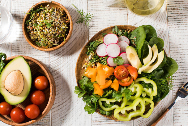 Gemüsesommersalat mit Avocado, saisonalem Gemüse, Spinat und Mikrogemüse auf weißem Holzgrund.  - Foto, Bild