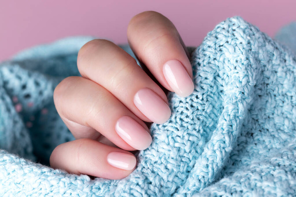Female hand in blue knitted sweater with beautiful natural manicure - pink nude nails. Nail care concept - Foto, Bild