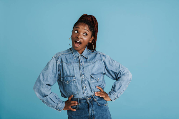 Young black woman with afro pigtails expressing surprise at camera isolated over blue background - Fotó, kép
