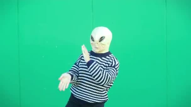 緑の壁にポーズをとった普段着のエイリアンマスクの人 - 映像、動画