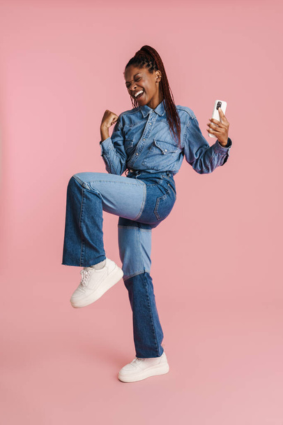 Excited black woman gesturing and using mobile phone isolated over pink background - Foto, immagini