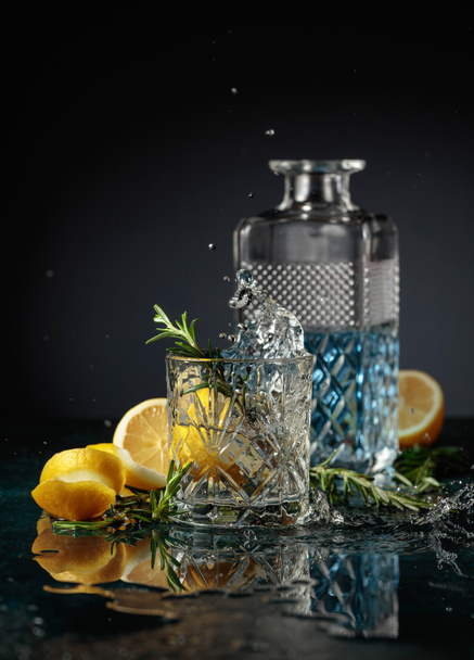 Cocktail gin tonique au citron et romarin. Tranche de citron tomber dans un verre avec un cocktail. - Photo, image