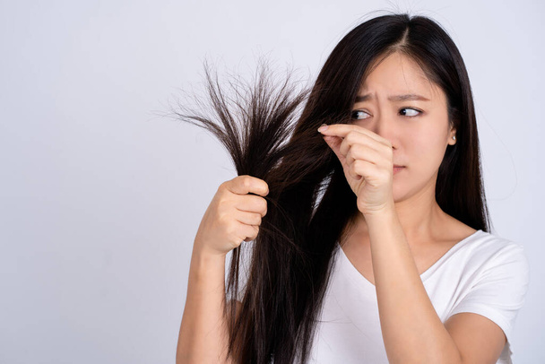 Mujer asiática con el pelo dañado. Ella está estresada y preguntándose algo aislado sobre un fondo blanco. - Foto, Imagen
