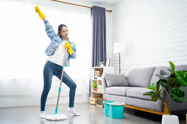 Happy woman sings while cleaning the living room using a mop as a microphone. She had fun while doing housework. - Фото, зображення