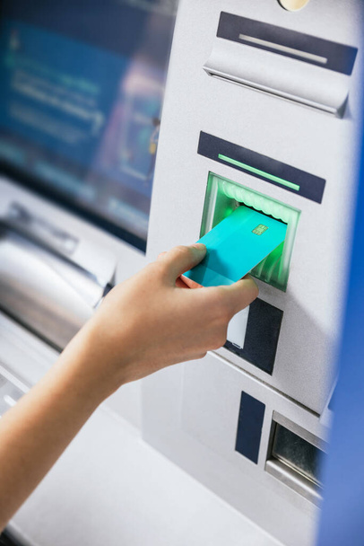 ATMの銀行のマシンにクレジットカードを挿入する若い女性の手のクローズアップは、お金を転送または引き出します。金融顧客と銀行サービスの概念。縦射 - 写真・画像