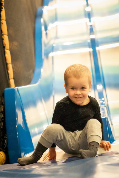 Little toddler boy sliding on shiny metal slide in amusement park at shopping mall - Photo, Image