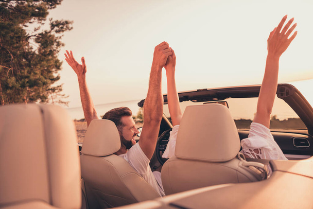 Photo of pretty charming married couple dressed white clothes driving car holding rising arms outdoors country side road - Фото, зображення