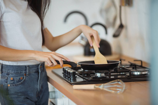 Щаслива приваблива молода домогосподарка готує їжу на сковороді на плиті для смачної вечері на сучасній кухні в стилі лофт. крупним планом
 - Фото, зображення
